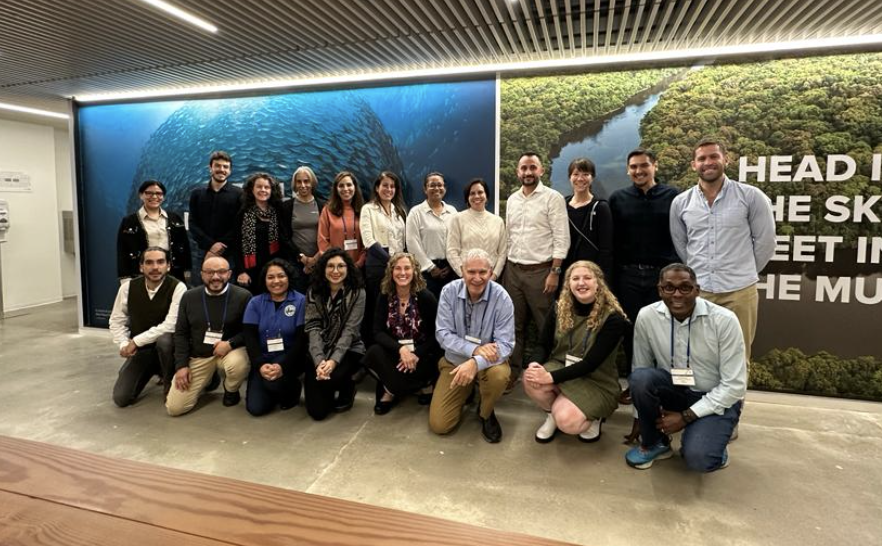 Course participants, staff, and instructors smile in front of a large wall with images of nature at Conservation international's headquarters.