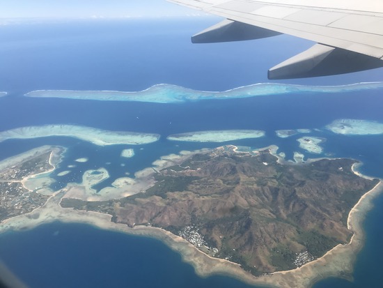 View from airplane on a flight from Fiji to the Solomon Islands. Shows green island, blue ocean, and airplane wing. 